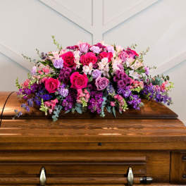 Large pink and purple floral arrangement on a wooden casket