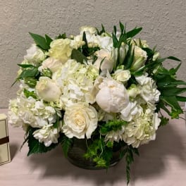Low round arrangement of white roses, hydrangeas, and peonies in a glass vase