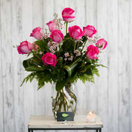 Arrangement of hot pink roses with tiny pink filler flowers in a clear glass vase.