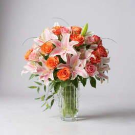 Pink lilies and orange roses arranged in a clear glass vase