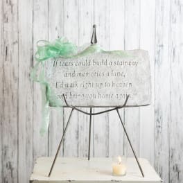 Memorial stone plaque on a metal stand with a green ribbon and candle