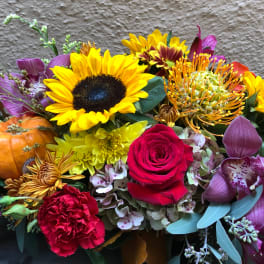 Mixed floral arrangement with sunflowers, roses, orchids, and a small pumpkin