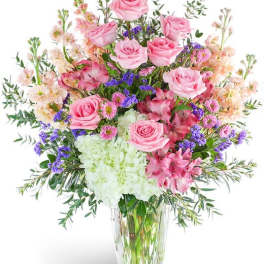 Pink roses and mixed flowers arranged in a clear glass vase