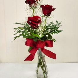 Three red roses in a clear glass vase with a red ribbon