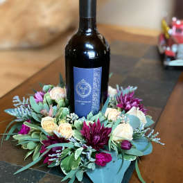 Wine bottle surrounded by a floral wreath of cream and purple flowers