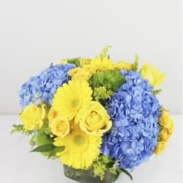 Blue hydrangeas and yellow roses in a square glass vase