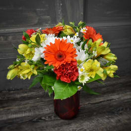 Mixed bouquet of orange, yellow, white, and red flowers in a red vase
