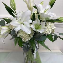 White lilies and hydrangeas arranged in a clear glass vase
