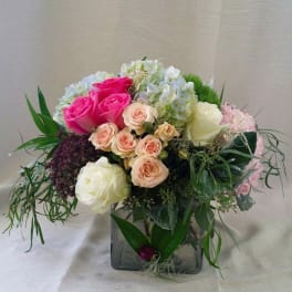 Mixed bouquet of pink, white, and peach roses in a square glass vase