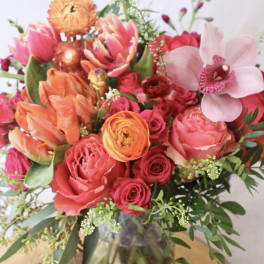 Mixed bouquet of pink, orange, and red flowers in a glass vase