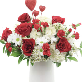 Red roses and white flowers in a white vase with heart picks