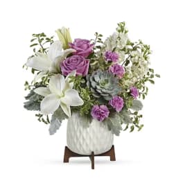 Bouquet of white lilies, purple roses, and succulents in a white vase
