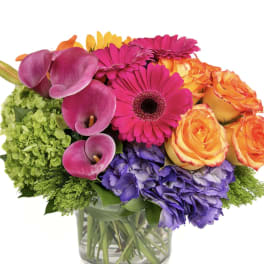 Colorful bouquet with roses, gerbera daisies, calla lilies, and hydrangeas in a glass vase