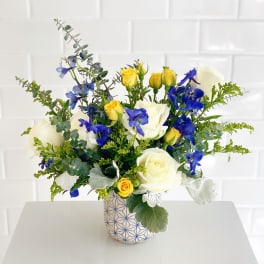 White and yellow roses with blue flowers in a patterned vase
