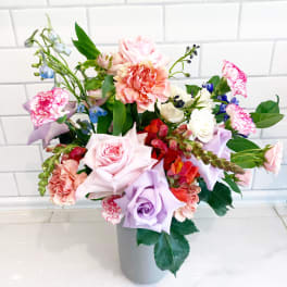 Mixed bouquet of pastel roses, carnations, and blue flowers in a gray vase