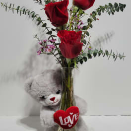 Red roses in a glass vase with a teddy bear and heart decoration