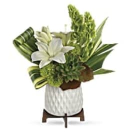 White lily arrangement with green tropical foliage in a white vase