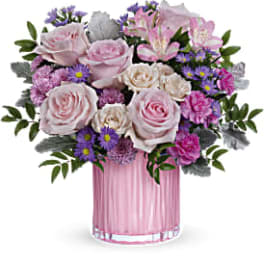 Pink and white roses with purple flowers in a pink glass vase