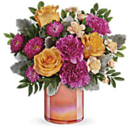 Bouquet of yellow roses, purple carnations, and peach flowers in a glass vase