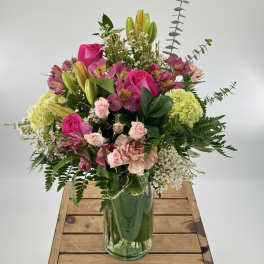 Tall mixed bouquet with pink roses, lilies, and green hydrangeas in a clear glass vase