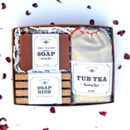 Gift box with soap, soap dish, and tub tea surrounded by rose petals