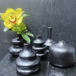 Yellow orchid in a small black vase with several black ceramic vases