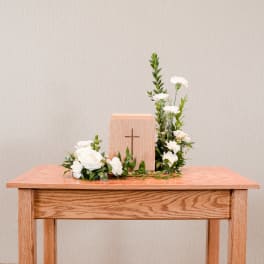 White floral arrangement around a wooden cross on a table