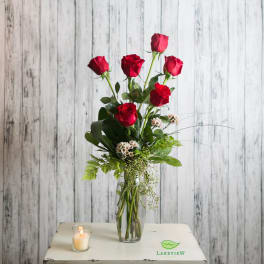 Red roses in a clear vase with a lit candle beside them