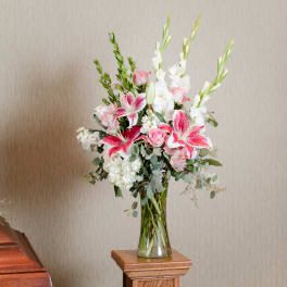 Tall bouquet of pink lilies, roses, and white flowers in a glass vase.