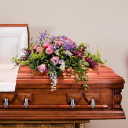 Casket spray of pink and purple flowers on a wooden casket