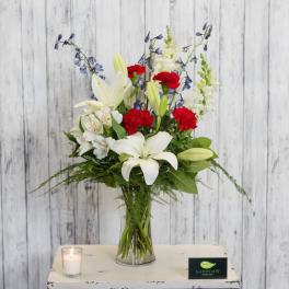 White lilies and red carnations in a glass vase with a lit candle