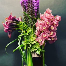 Tall arrangement of pink orchids, purple flowers, and green succulents in a vase