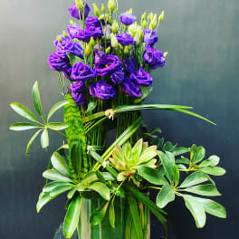 Purple lisianthus arrangement in a clear glass vase with green foliage