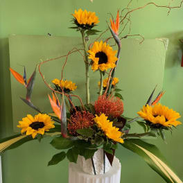 Tall floral arrangement with sunflowers and orange bird-of-paradise in a white vase