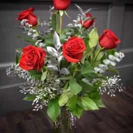 Red roses arranged in a clear glass vase with silver foliage