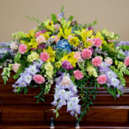 Colorful floral casket spray with yellow, pink, and lavender flowers