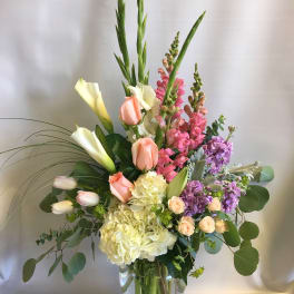 Tall mixed bouquet with calla lilies, roses, hydrangeas, and snapdragons in a glass vase