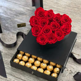 Heart-shaped red rose arrangement on a black gift box with gold chocolates