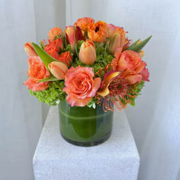 Orange roses and tulips arranged in a green glass vase