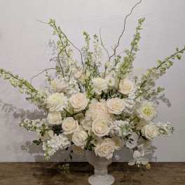 White floral arrangement in a white pedestal vase with tall branching stems