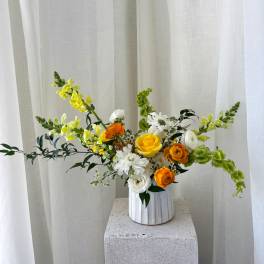 Yellow, white, and orange flowers in a white vase