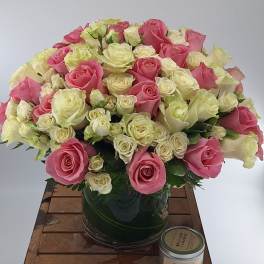 Pink and white roses arranged in a glass vase on a wooden table