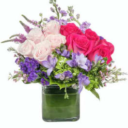 Pink and white roses with purple flowers in a green glass vase