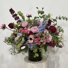Large mixed bouquet in a dark green vase with pink, burgundy, and blue flowers