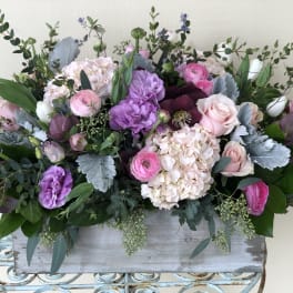 Low pastel arrangement of pink and purple flowers in a rustic rectangular wooden box