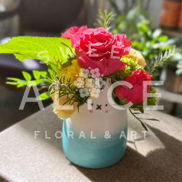 Small pink and yellow flower arrangement in a teal and white animal-face ceramic vase