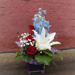 Red roses and a white lily with blue flowers in a square vase