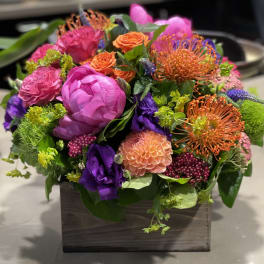 Bright mixed arrangement of pink, orange, purple, and green flowers in a low wooden box