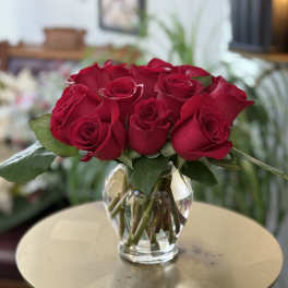 Compact arrangement of red roses in a clear glass vase on a small round table