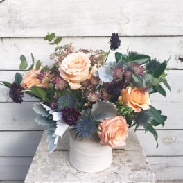 Peach roses and thistle in a white vase